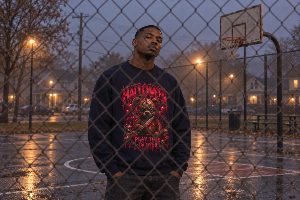 Model wearing the navy Playtime Is Over teddy bear sweatshirt behind a chain-link fence at a foggy neighborhood basketball court.